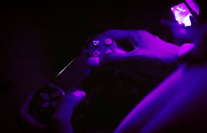 A close-up shot of hands gripping a gaming controller, illuminated by purple light, creating a vibrant atmosphere.