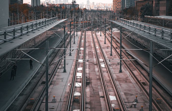 An aerial view of a modern railway station with tracks extending into the cityscape at dusk.