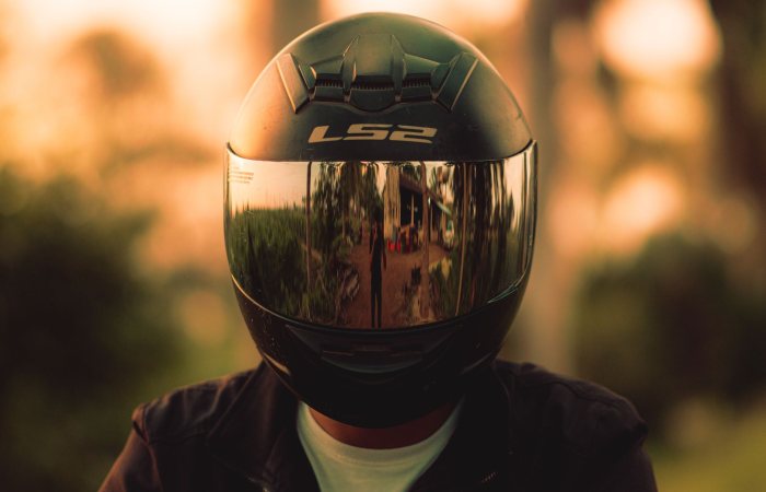 Close-up of a motorcyclist wearing a reflective helmet, capturing outdoor reflections during sunset.