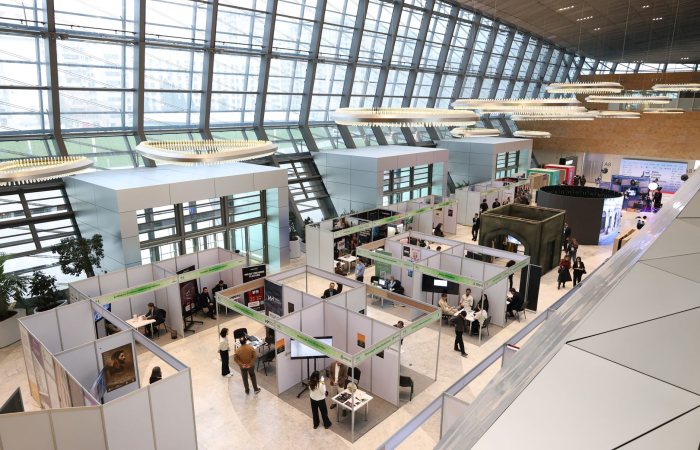 A bustling trade show exhibition inside a modern hall with people networking and exploring booths.