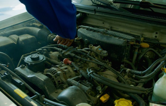 Mechanic in blue uniform working on a car engine in a garage environment.